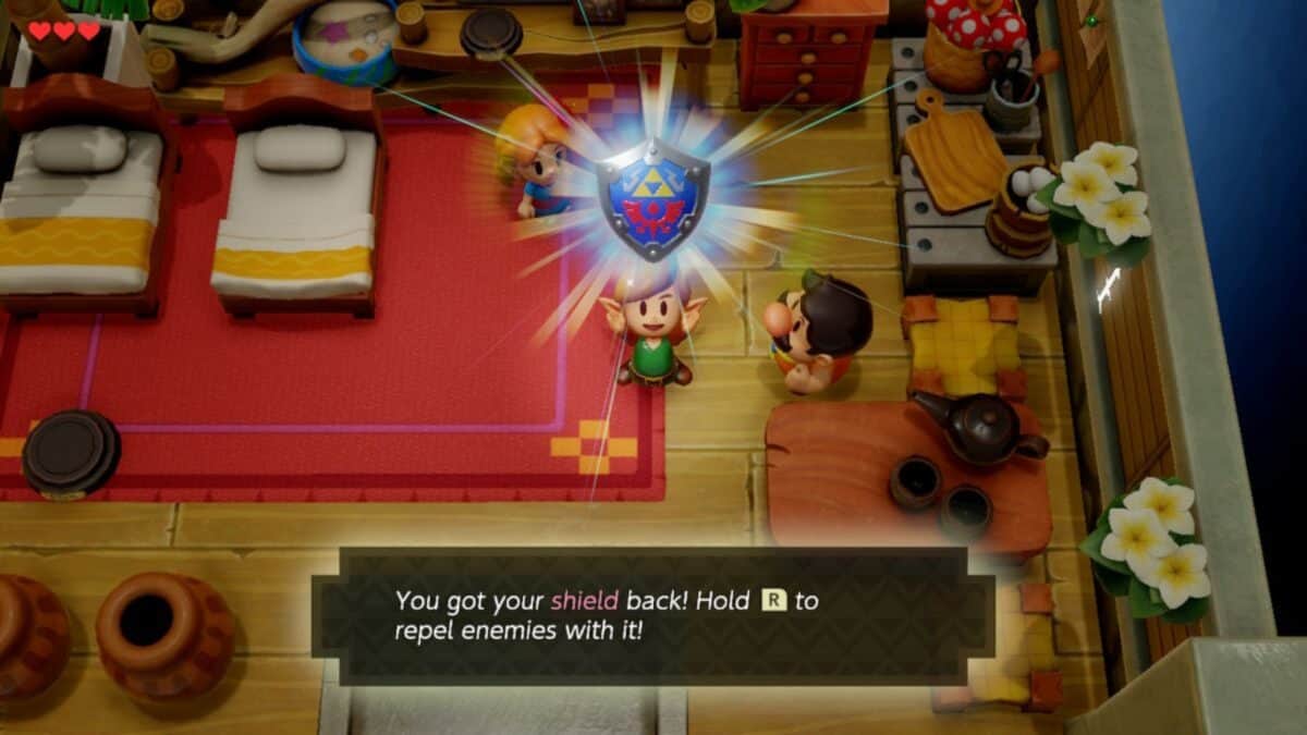 A character rejoices while holding a glowing shield in a room with beds, pots, and people. A message reads, "You got your shield back! Hold R to repel enemies with it!.