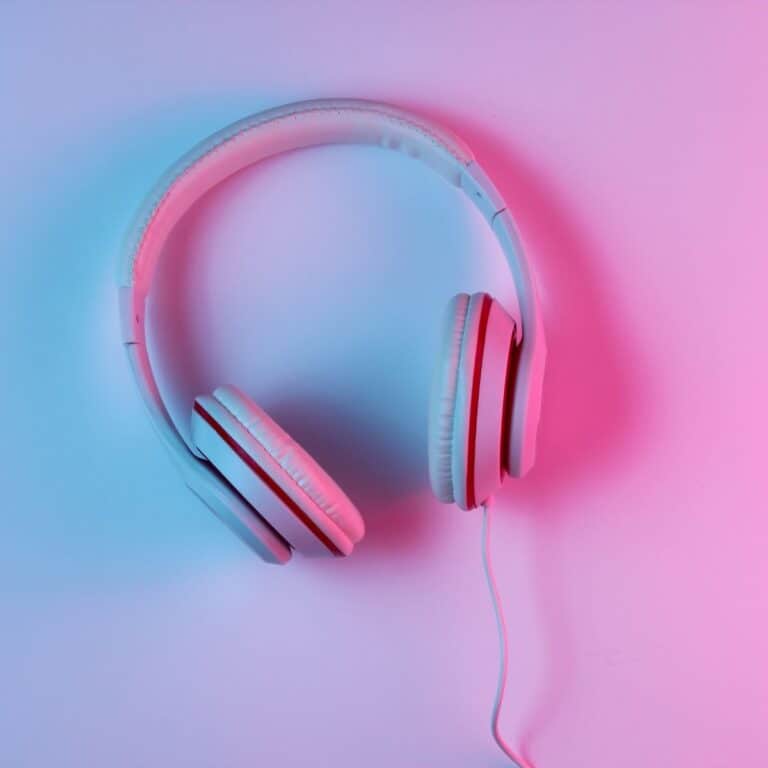 White over-ear headphones with a wired connection are placed on a flat surface, illuminated by blue and pink lighting—an eye-catching pick for those seeking the best headphones for gaming.