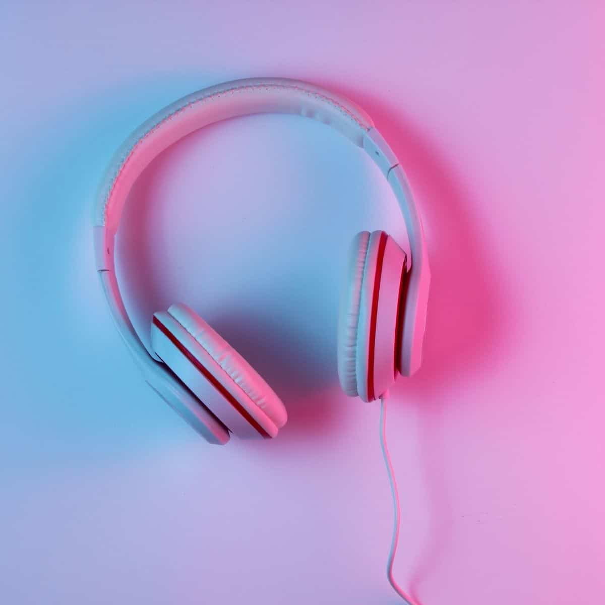White over-ear headphones with a wired connection are placed on a flat surface, illuminated by blue and pink lighting—an eye-catching pick for those seeking the best headphones for gaming.