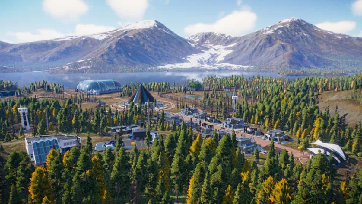 A modern facility with multiple buildings and domes is surrounded by forest, with a lake and snow-capped mountains in the background under a blue sky.