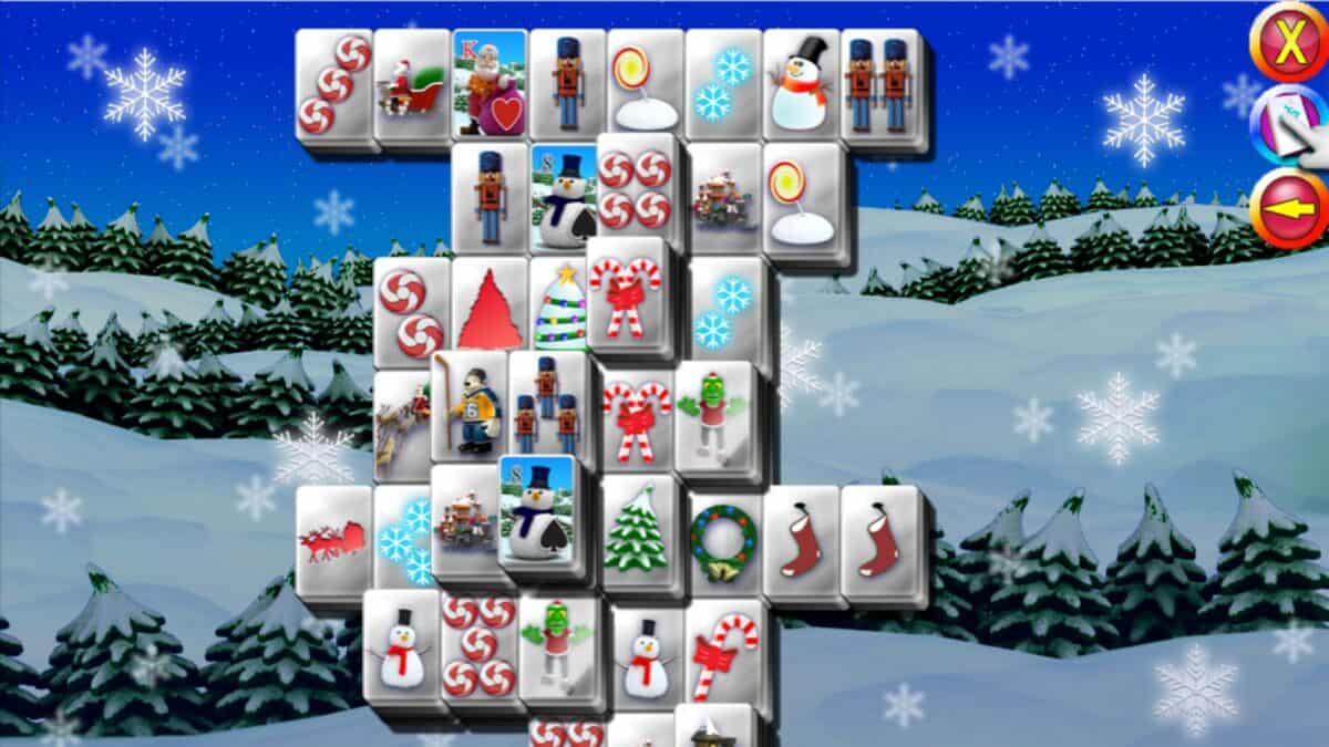 A digital Mahjong game with Christmas-themed tiles, including nutcrackers, snowmen, stockings, and candy, set against a snowy, nighttime forest background.