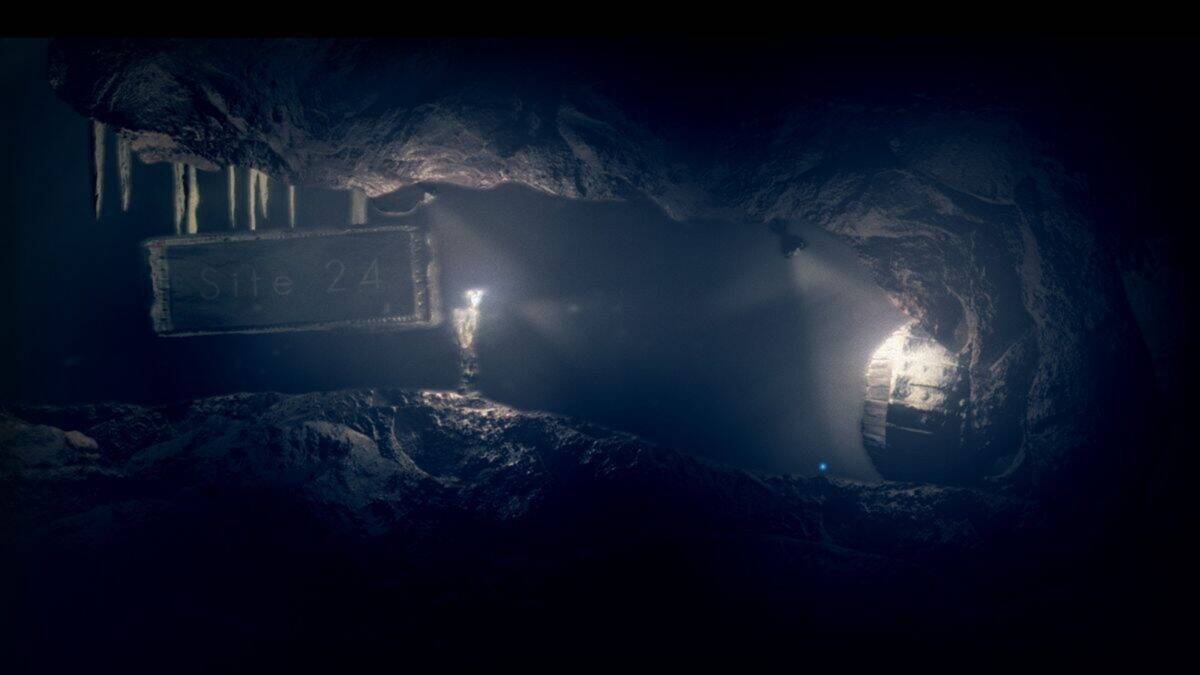 A dark underground cave with a worn sign reading "Site 24," illuminated by dim lights from a figure and a hanging lantern.