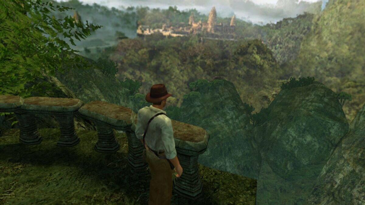 A man in a hat and suspenders stands on a stone terrace overlooking a dense jungle with ancient ruins visible in the distance.